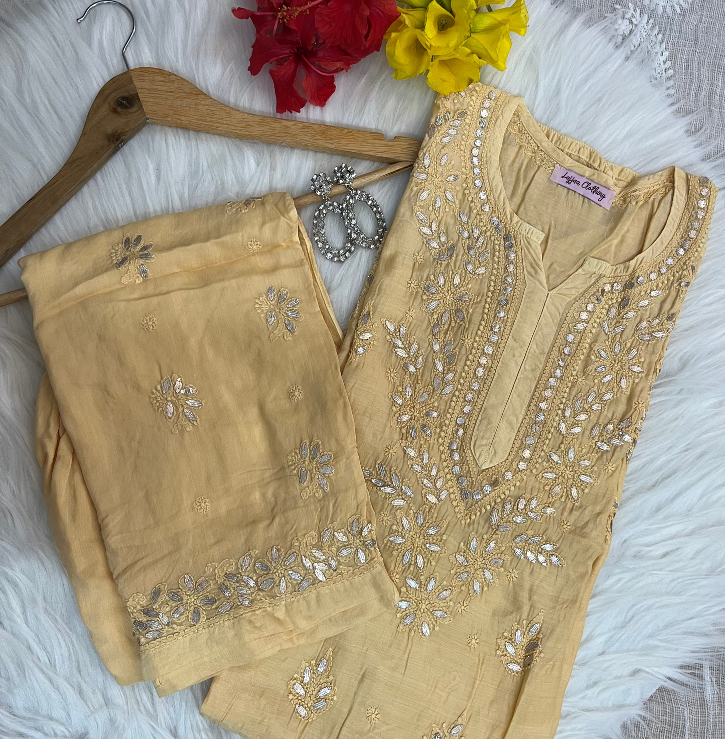 Beige embroidered outfit on a hanger with flowers and jewelry on a textured surface