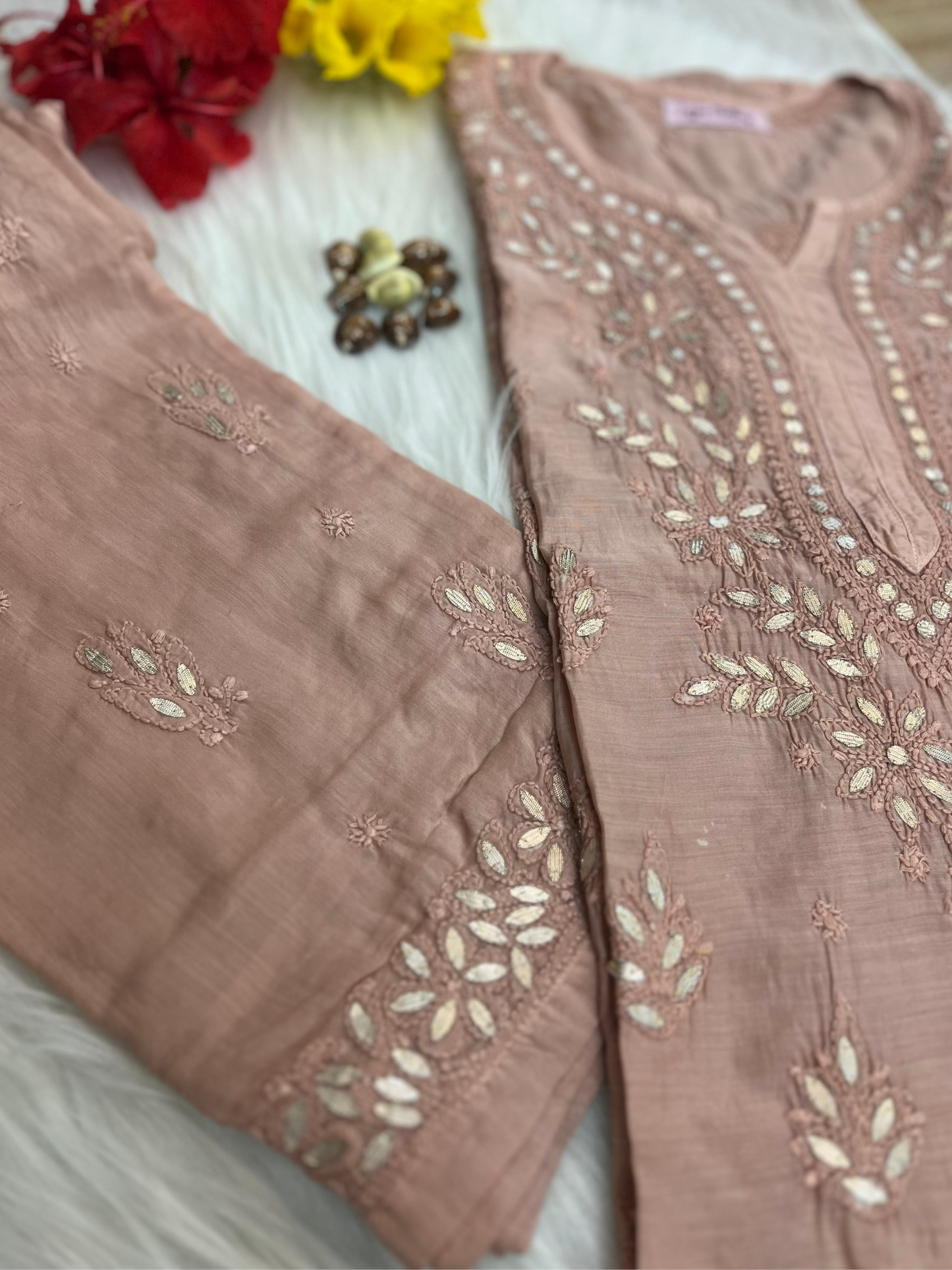 Brown embroidered fabric with floral patterns on a white surface with flowers and jewelry.