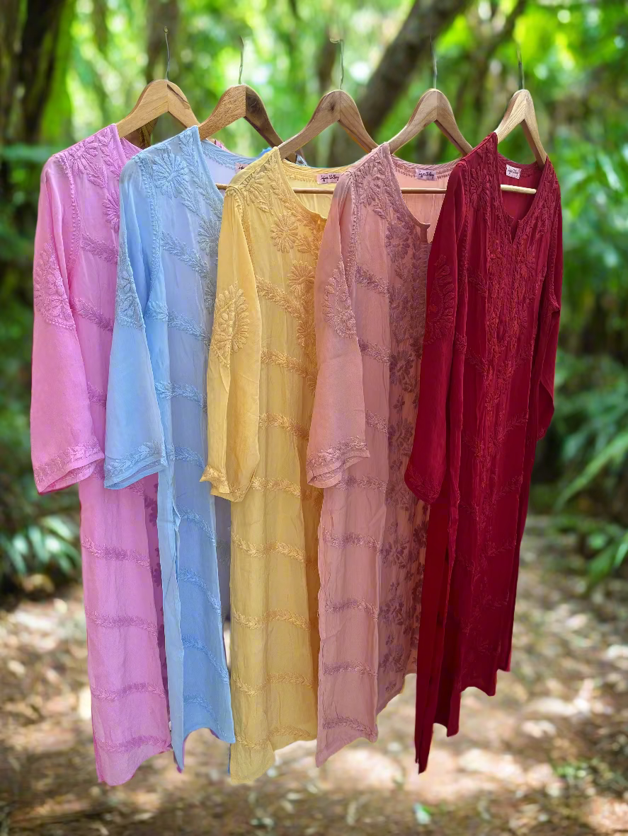 Five dresses in pink, blue, yellow, and red hanging on a rack outdoors.