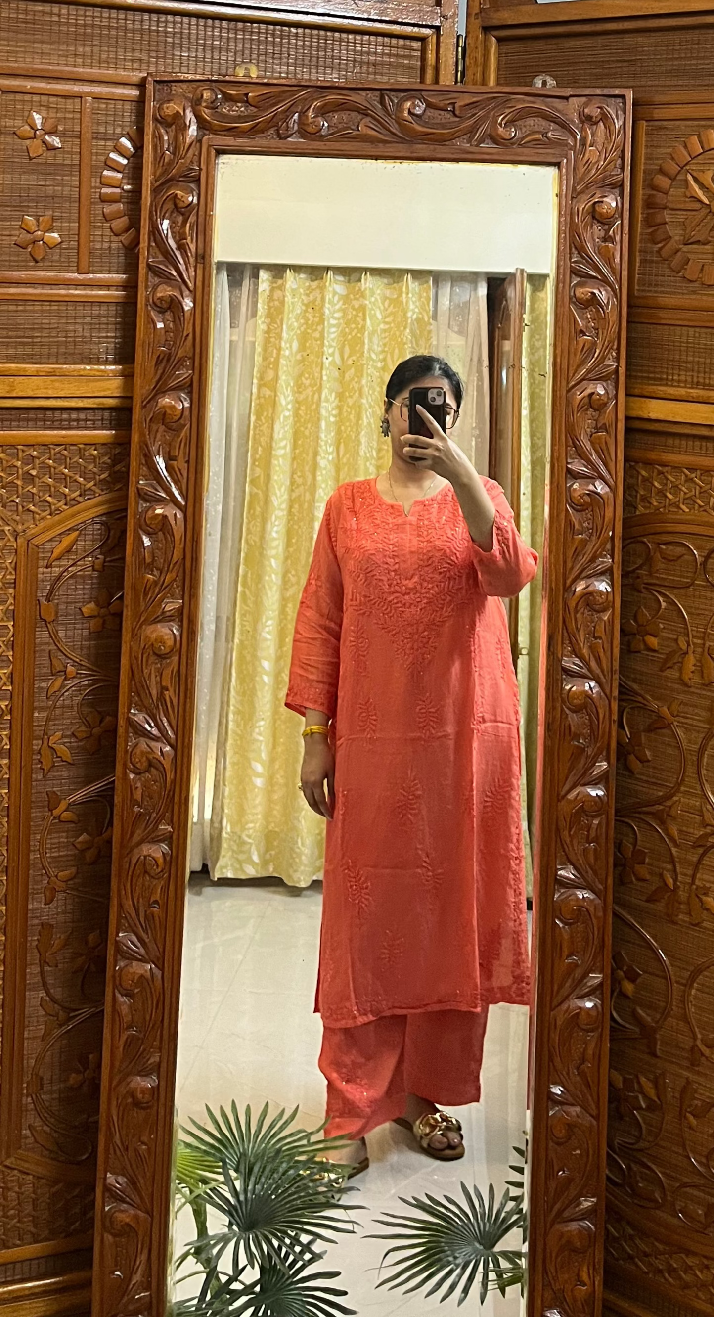 Person taking a mirror selfie in a room with a wooden screen and ceiling fan.