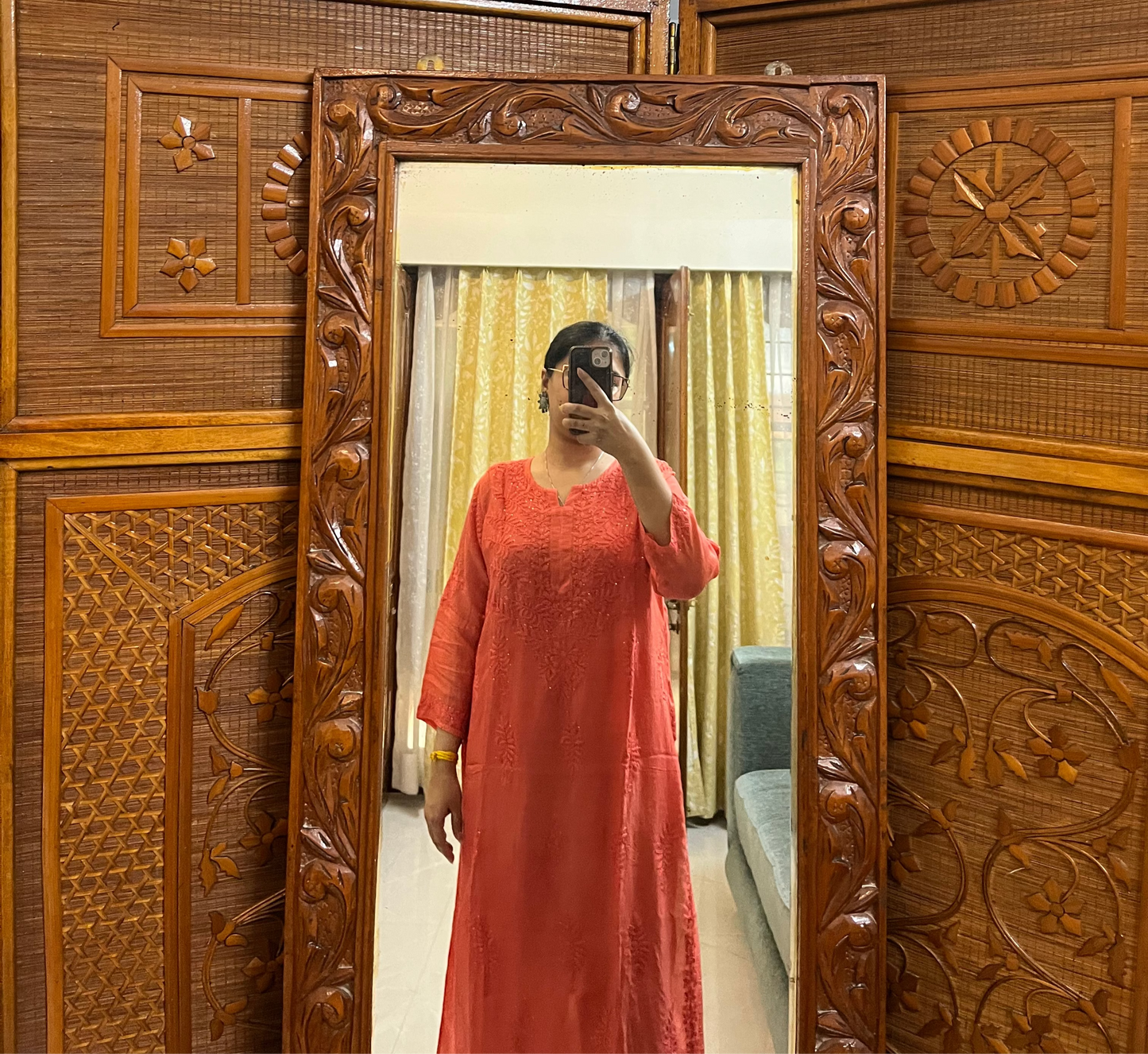 Person wearing a red dress standing in front of a wooden carved screen with a mirror.