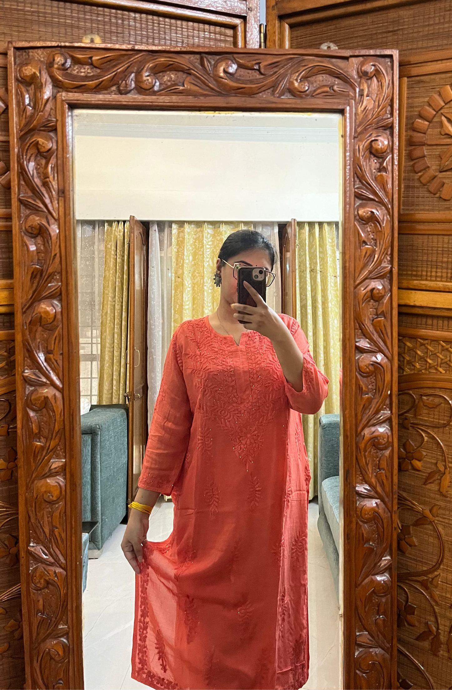 Person wearing a coral dress standing in front of a wooden carved mirror.