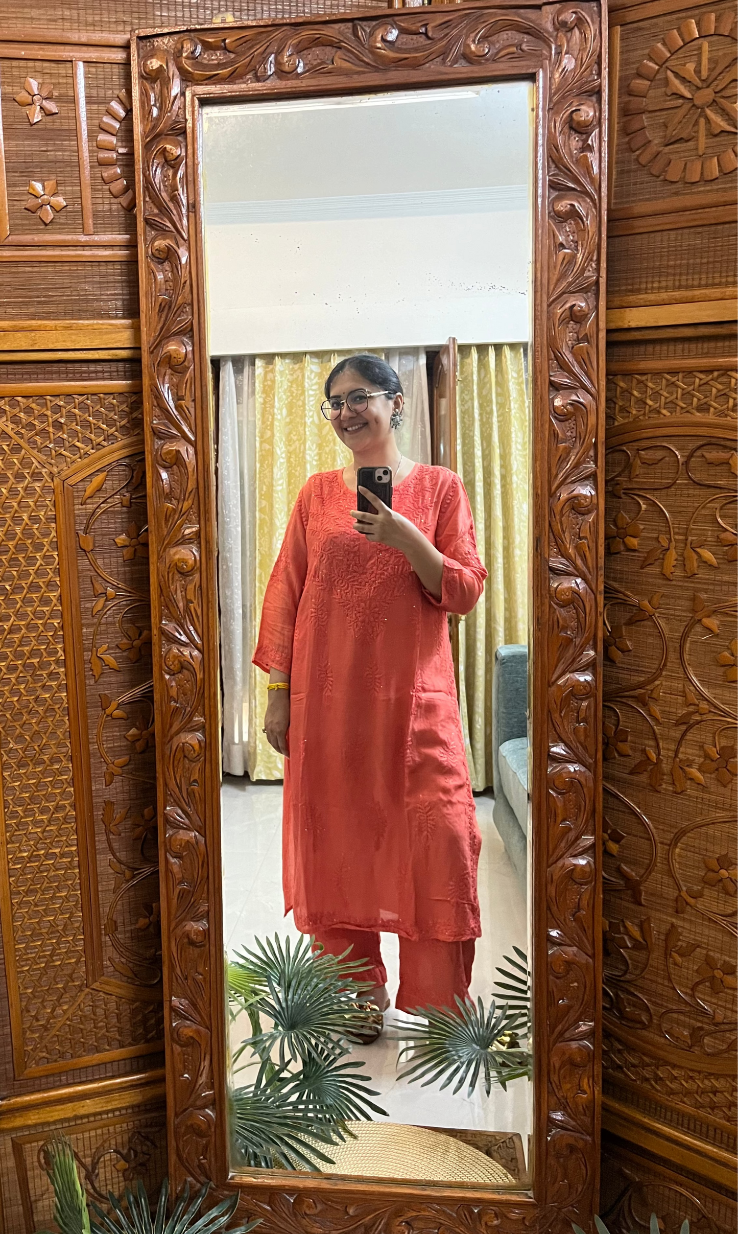 Person wearing a pink outfit standing in front of a decorative wooden mirror.