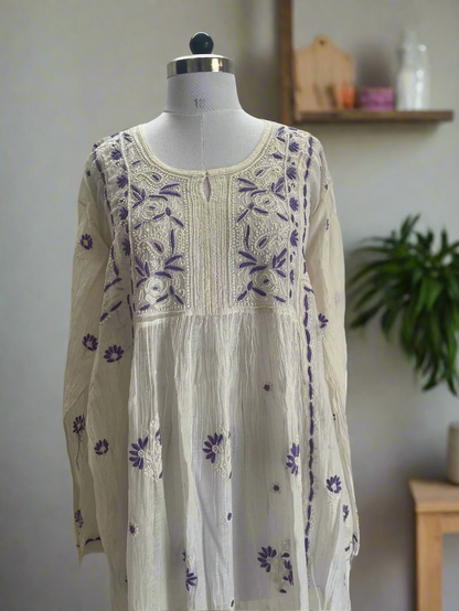 White dress with purple floral embroidery on a mannequin against a plain background
