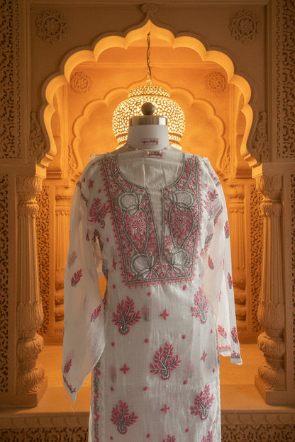 A white sheer embroidered tunic top displayed on a dress form mannequin, featuring pink and gray floral patterns and a detailed embroidered yoke, set against a window view.