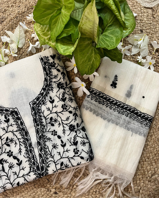 Two scarves with black floral patterns on a textured surface with green leaves and white flowers.