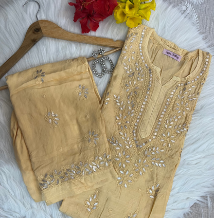 Beige embroidered outfit on a hanger with flowers and jewelry on a textured surface