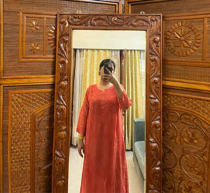 Person wearing a red dress standing in front of a wooden carved screen with a mirror.